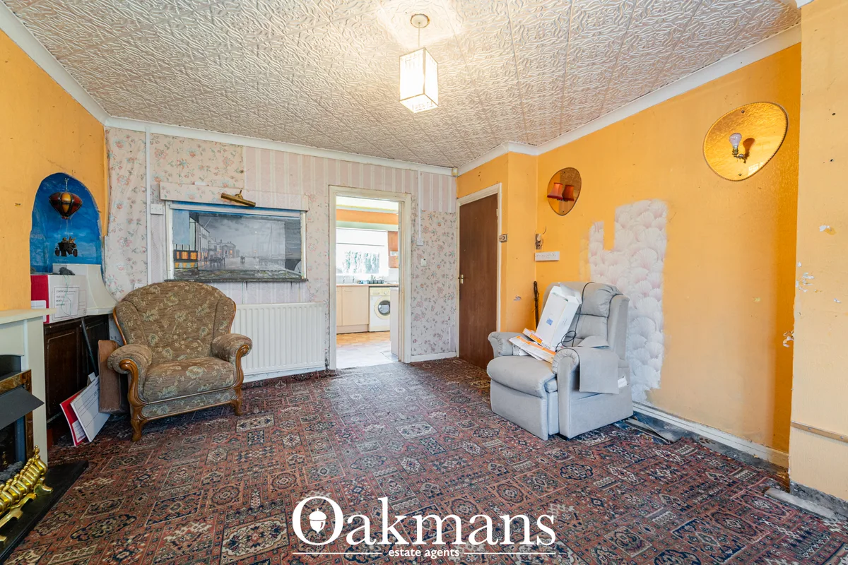Yellow-walled living room with patterned ceiling, two armchairs, ornate rug, fireplace and doorway to kitchen