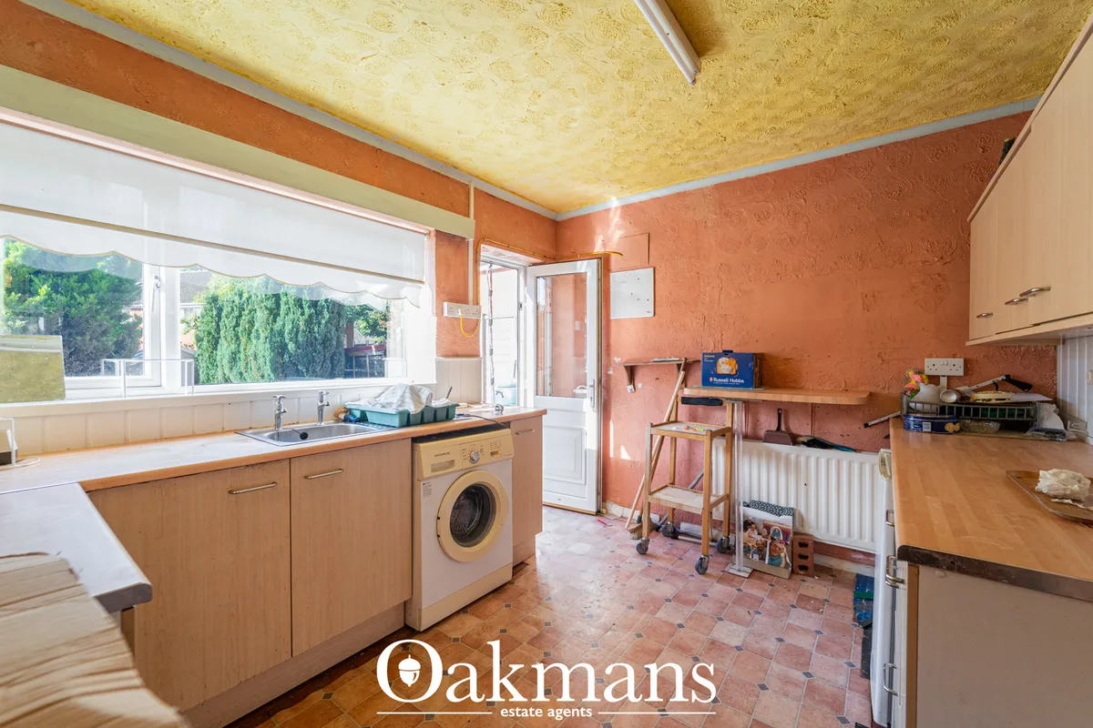 Kitchen with wooden units, washing machine, orange textured walls, cork ceiling, patio doors and bay window overlooking 
