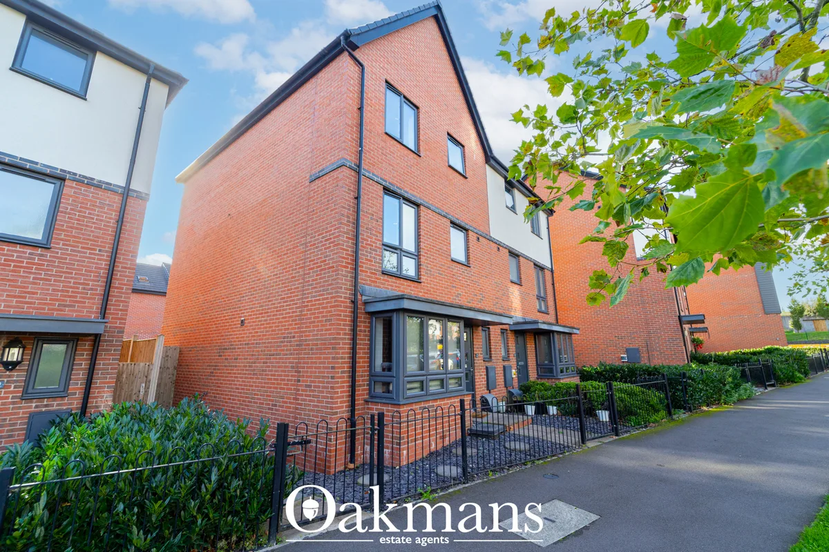 Modern red brick townhouse with pitched roof, large windows, black-framed entrance door, metal railings, and green climb