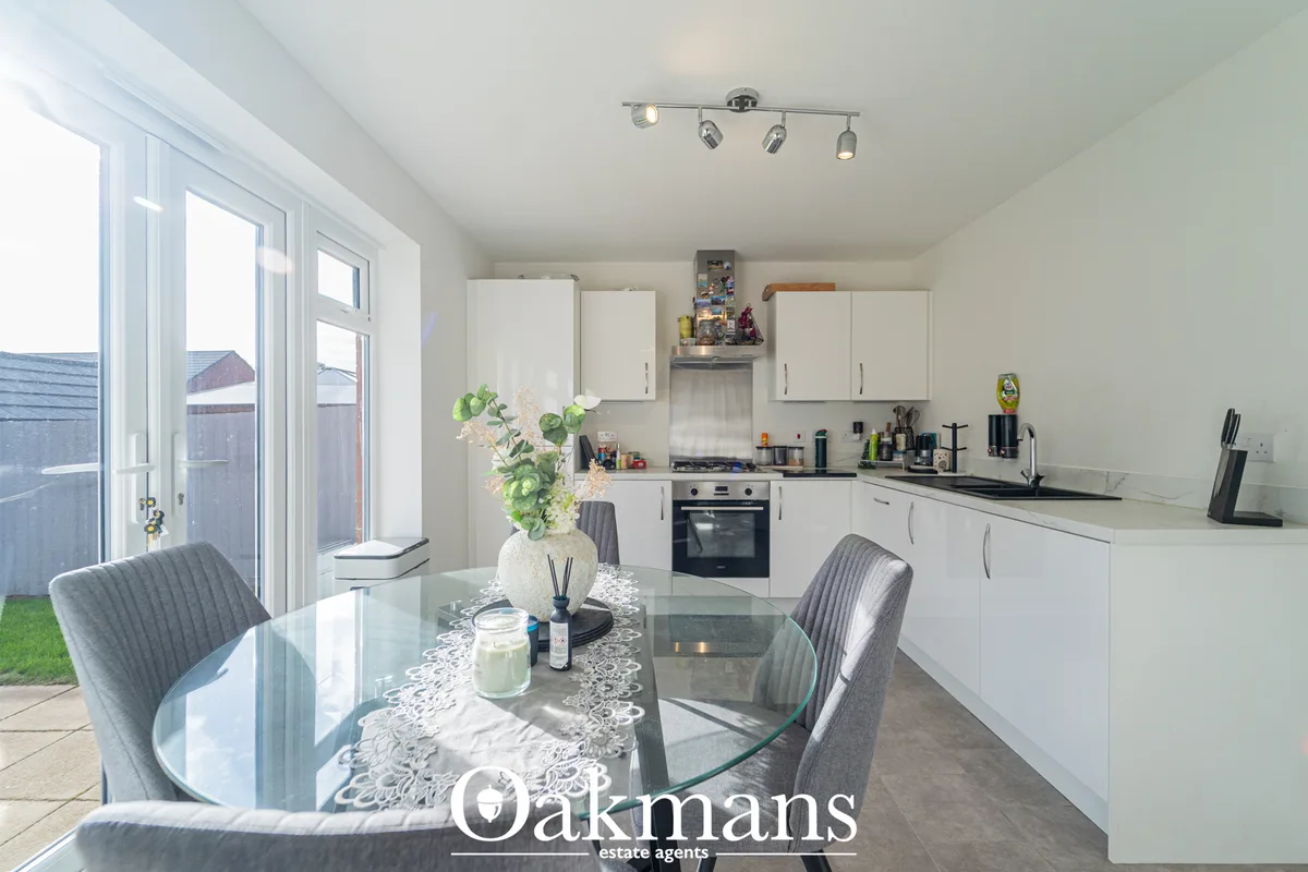 Modern fitted kitchen with white units, gas hob, integrated oven, and breakfast bar overlooking dining area with garden 