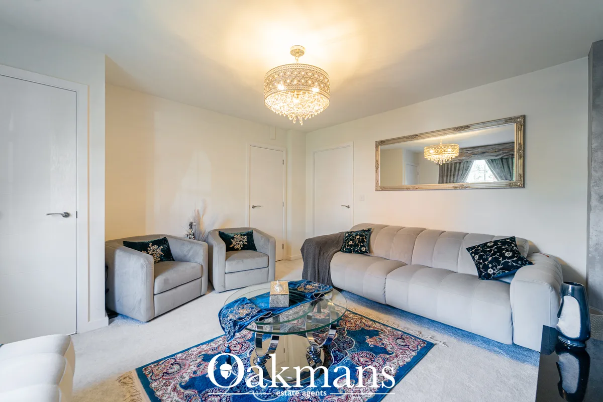 Elegant living room with cream sofa, matching armchairs, decorative navy cushions, glass coffee table on patterned rug, 