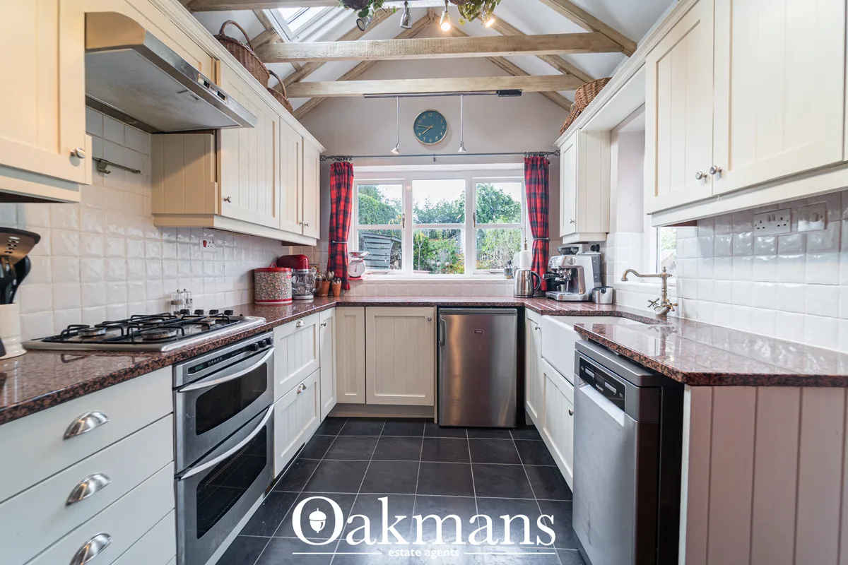 Modern fitted kitchen with white units, red granite worktops, stainless steel appliances, vaulted ceiling with exposed b