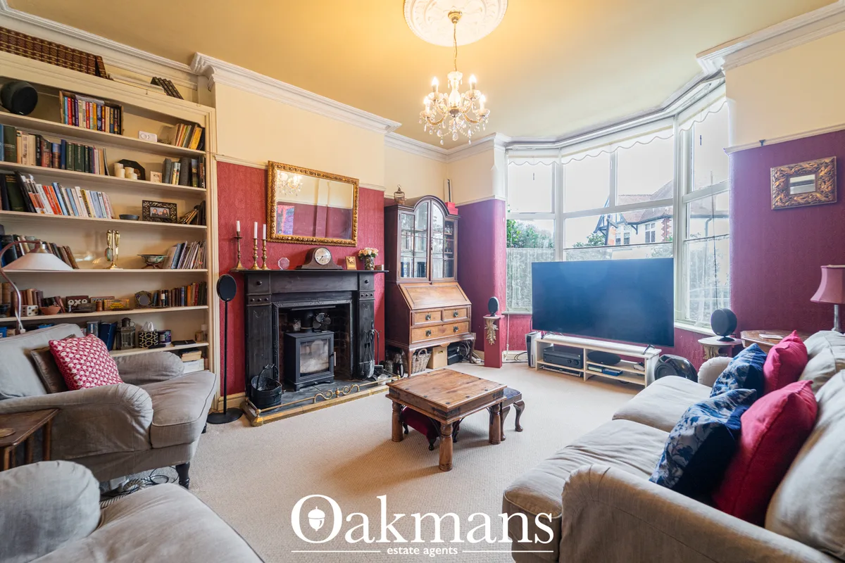 Spacious living room with cream carpet, cream sofa, fireplace with red feature wall, bookshelves, TV, chandelier and bay