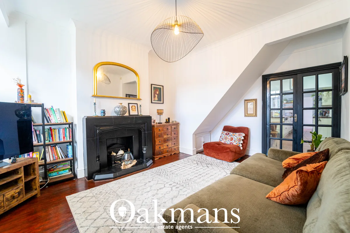 Spacious attic living room with sloped ceiling, fireplace, bookshelves, pendant light, and orange velvet seating