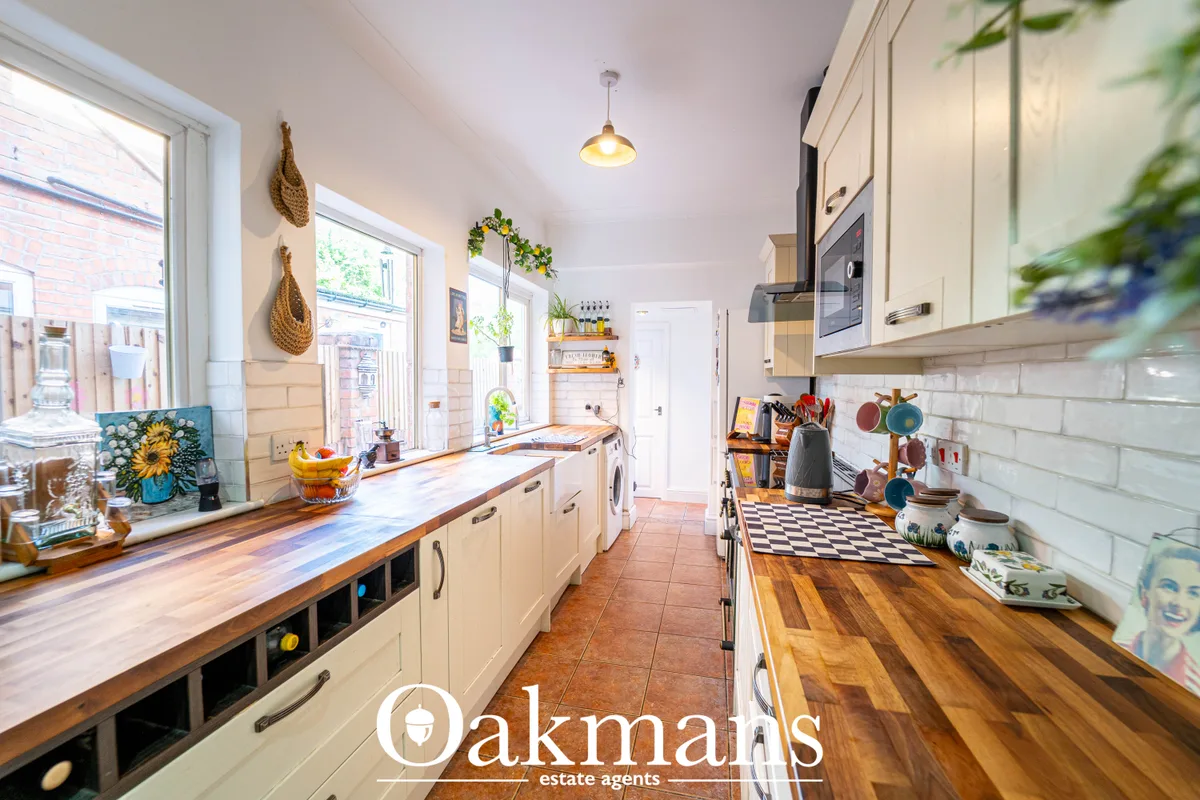 Galley kitchen with cream units, wooden worktops, white subway tile splashback, pendant lighting and black-and-white flo