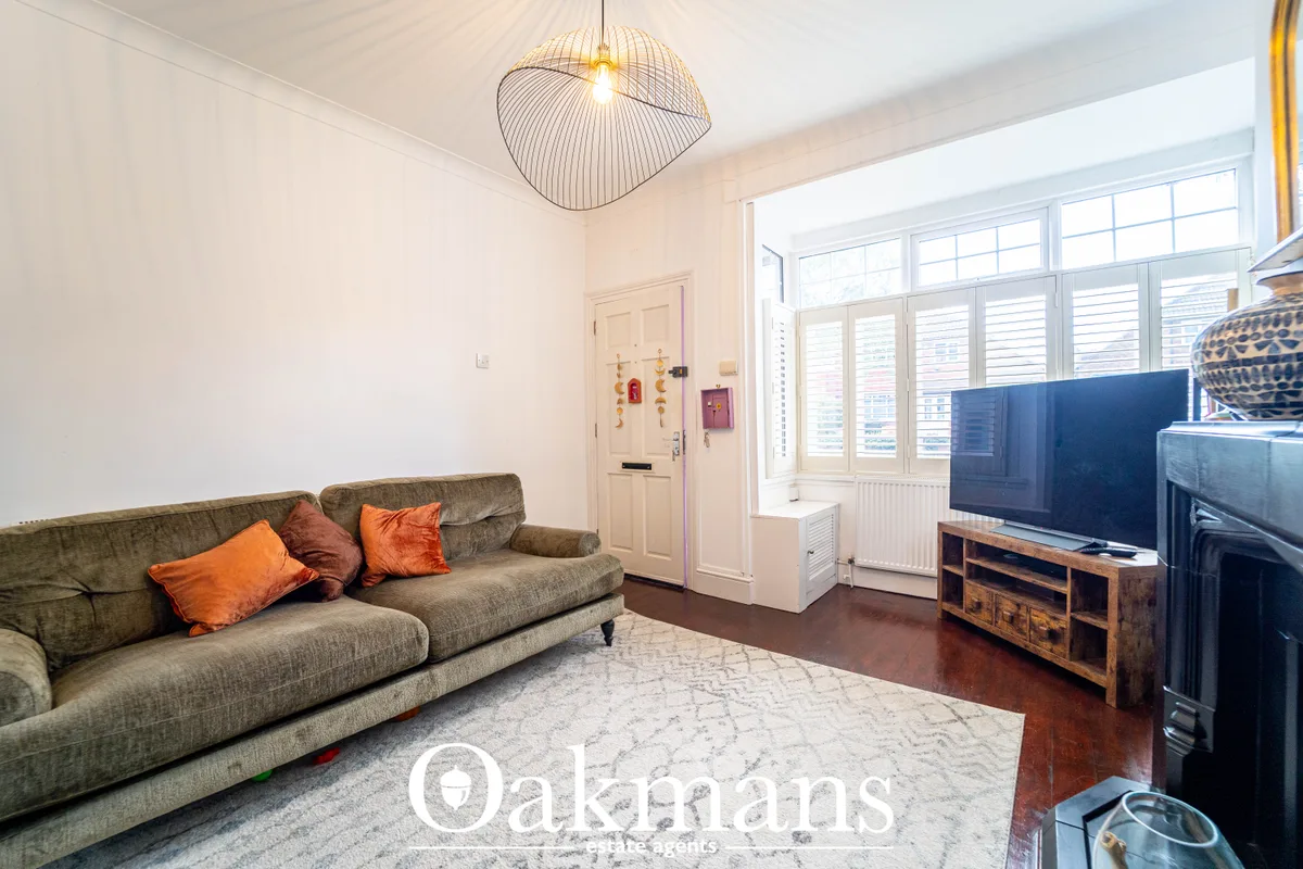Bright living room with olive-green sofa, orange cushions, wooden TV unit, pendant light, and large sash windows with sh