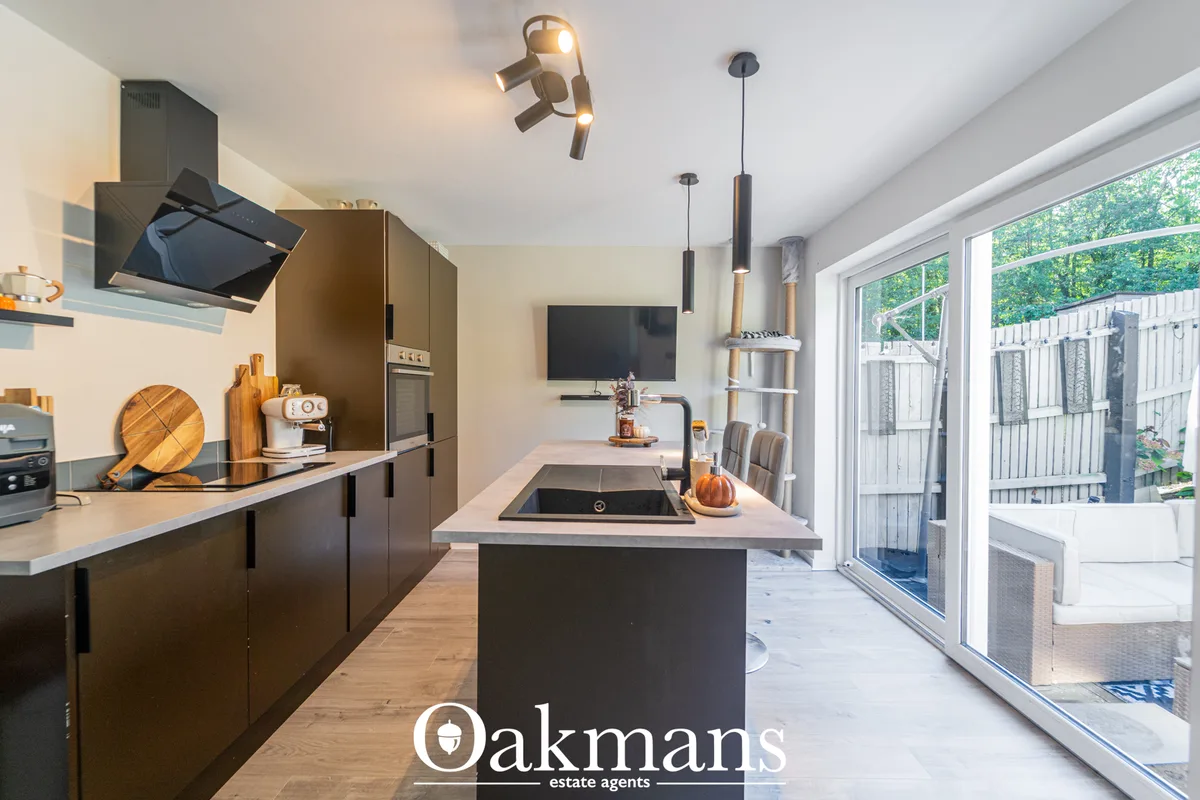 Modern open-plan kitchen with dark cabinetry, island with sink, pendant lighting, and sliding doors to garden