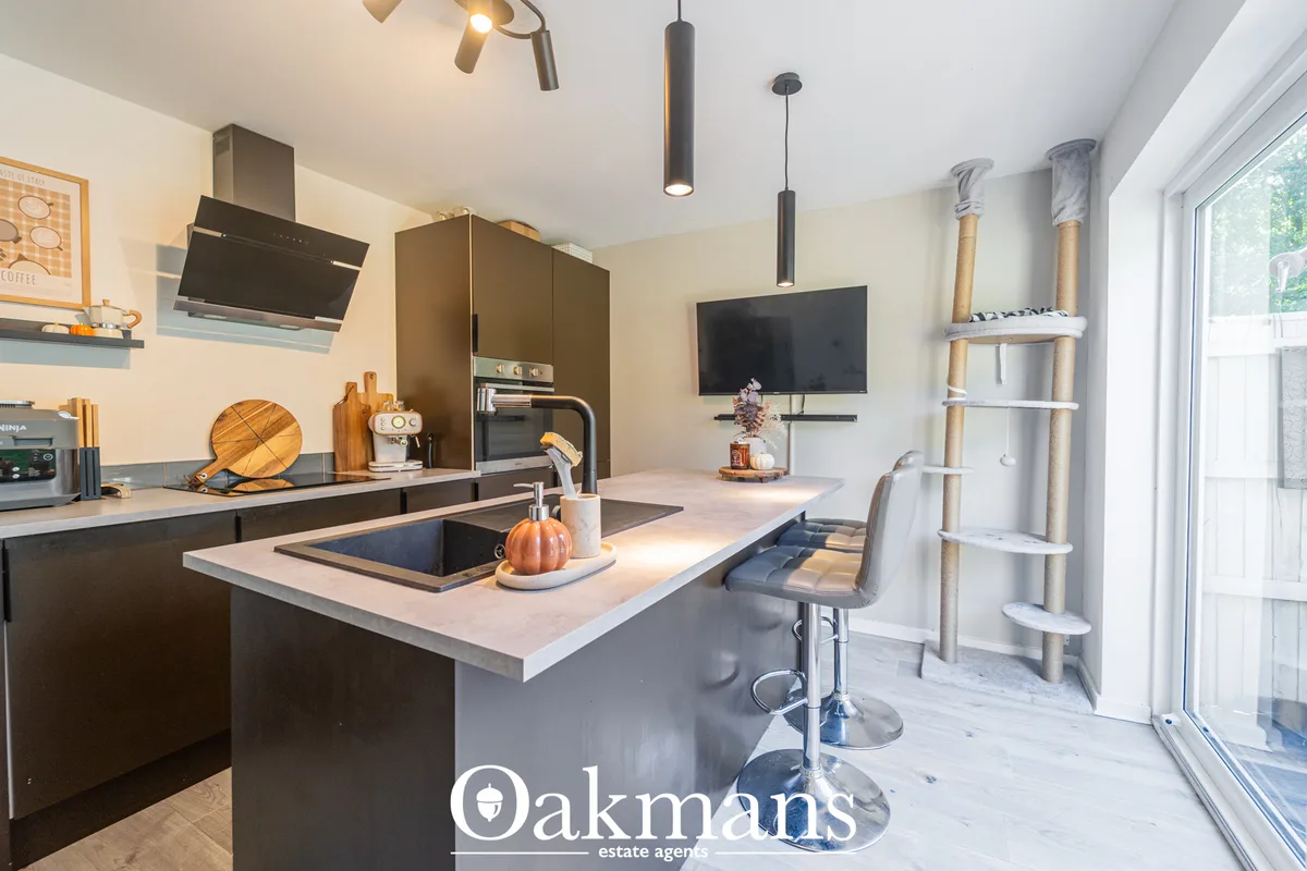 Modern open-plan kitchen with dark cabinetry, white worktops, island with breakfast bar seating, integrated appliances a