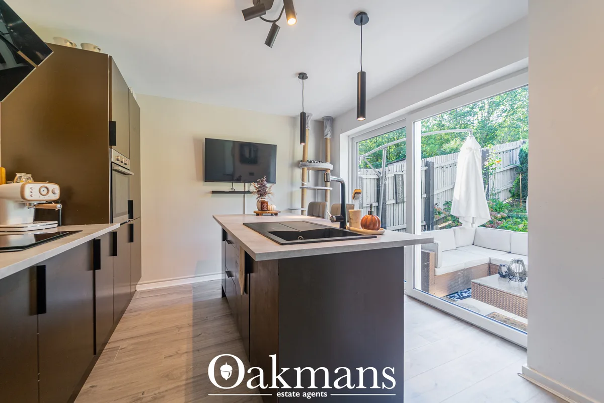 Modern kitchen with dark cabinetry, light worktops, island with induction hob, pendant lighting, and bi-fold doors openi
