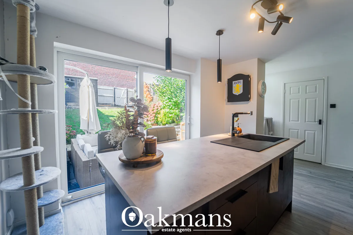 Modern kitchen with grey concrete island, pendant lights, patio doors opening to garden, cat tree, and contemporary fitt