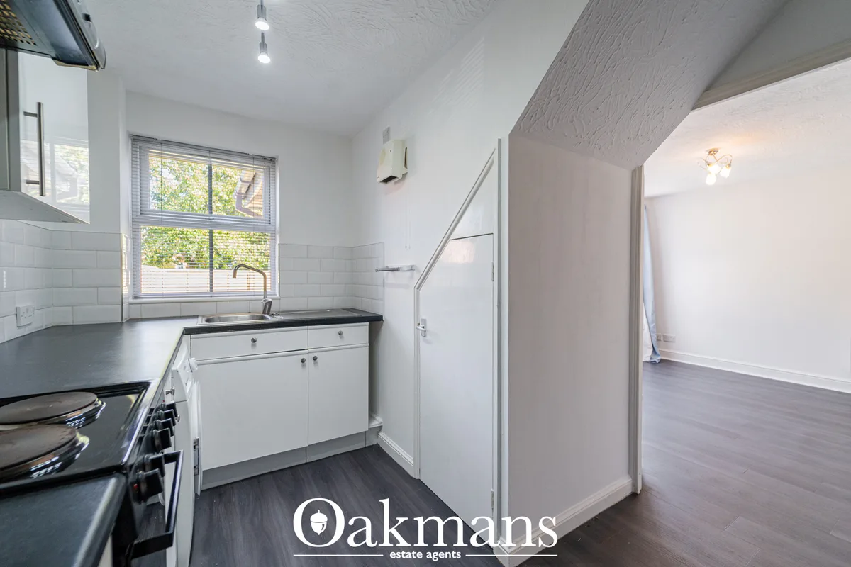 Modern fitted kitchen with white cabinetry, dark worktops, gas hob, window with views to garden, and open-plan access to