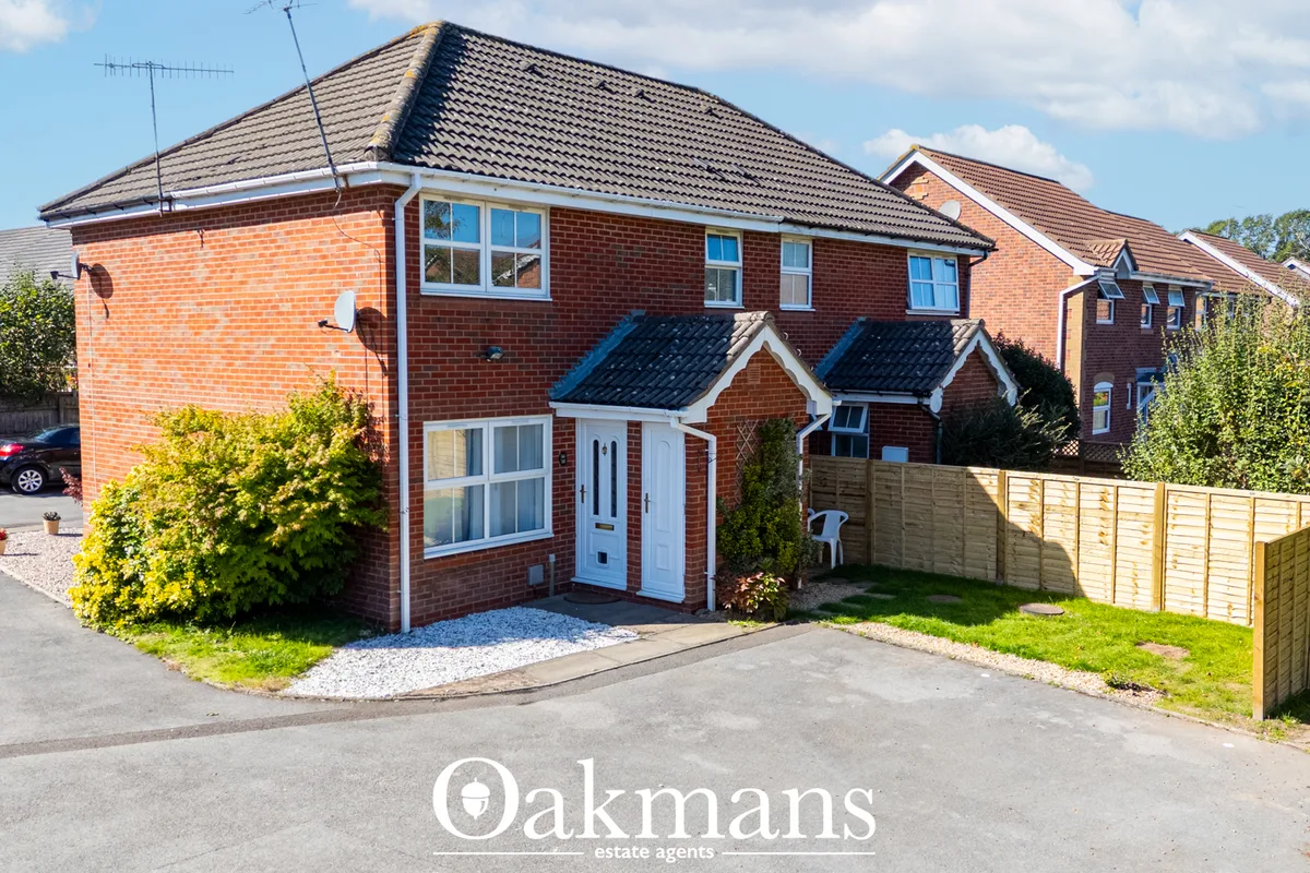 Red brick detached house with dark tiled roof, white door and windows, driveway with parked car and wooden fencing
