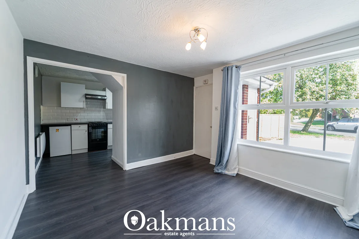 Open-plan living room with dark wood flooring, grey accent wall, white walls, large window with blue curtains overlookin