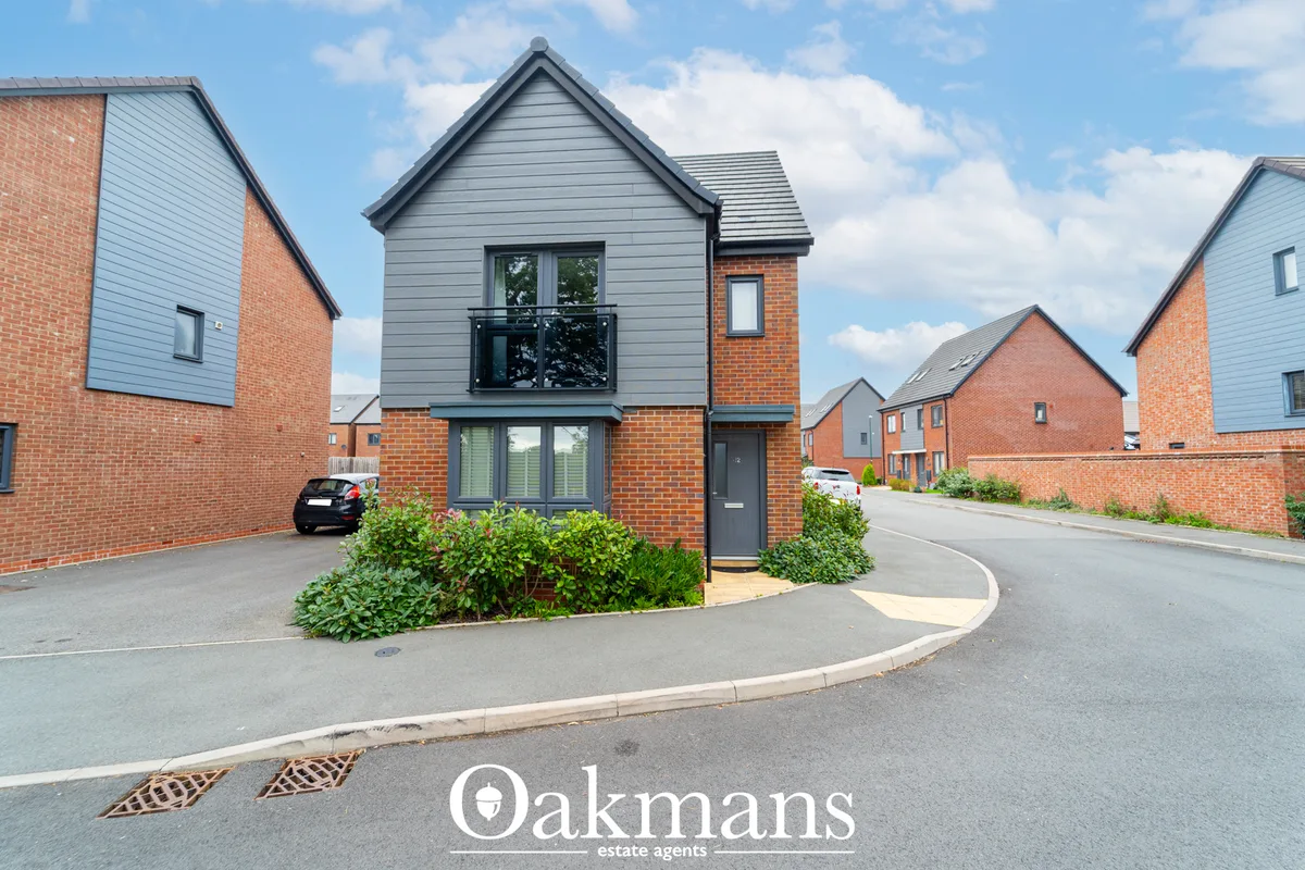 Modern brick-built house with grey cladding upper storey, pitched roof, front garden with hedging and parked car on driv
