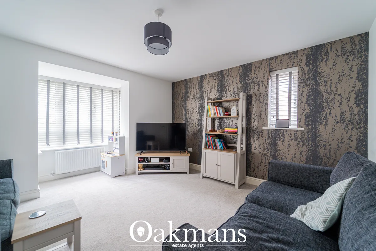 Spacious living room with grey upholstered sofa, patterned wallpaper accent wall, white shelving unit with books, TV on 