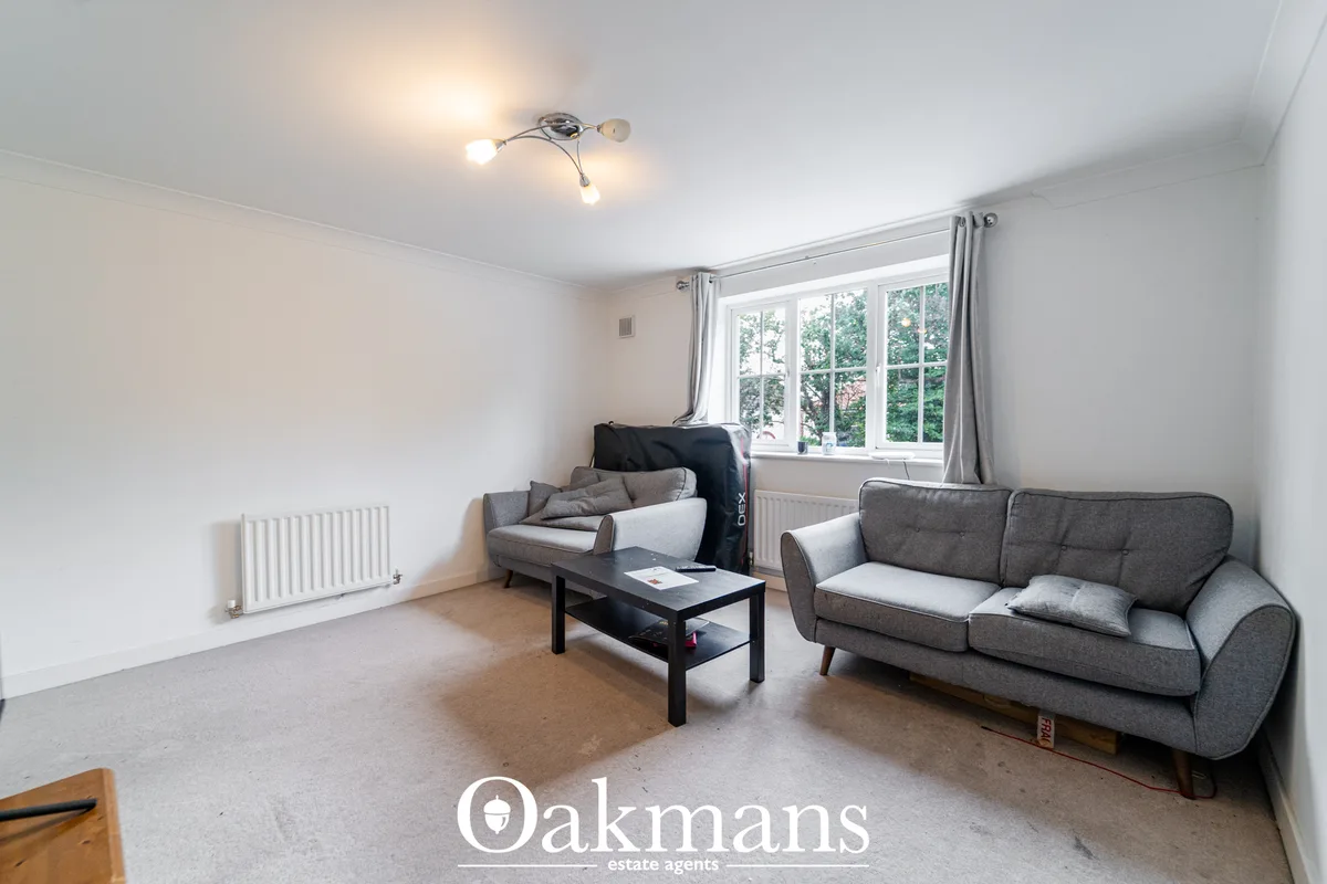 Bright living room with grey sofas, black coffee table, radiator and large multi-pane window overlooking greenery