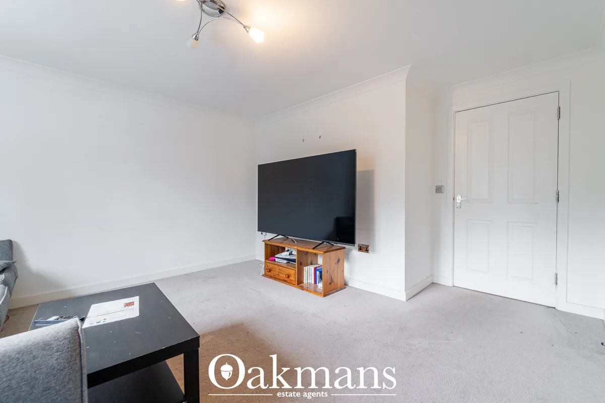 Spacious living room with cream carpet, white walls, wall-mounted flat-screen TV on wooden stand, black coffee table, an