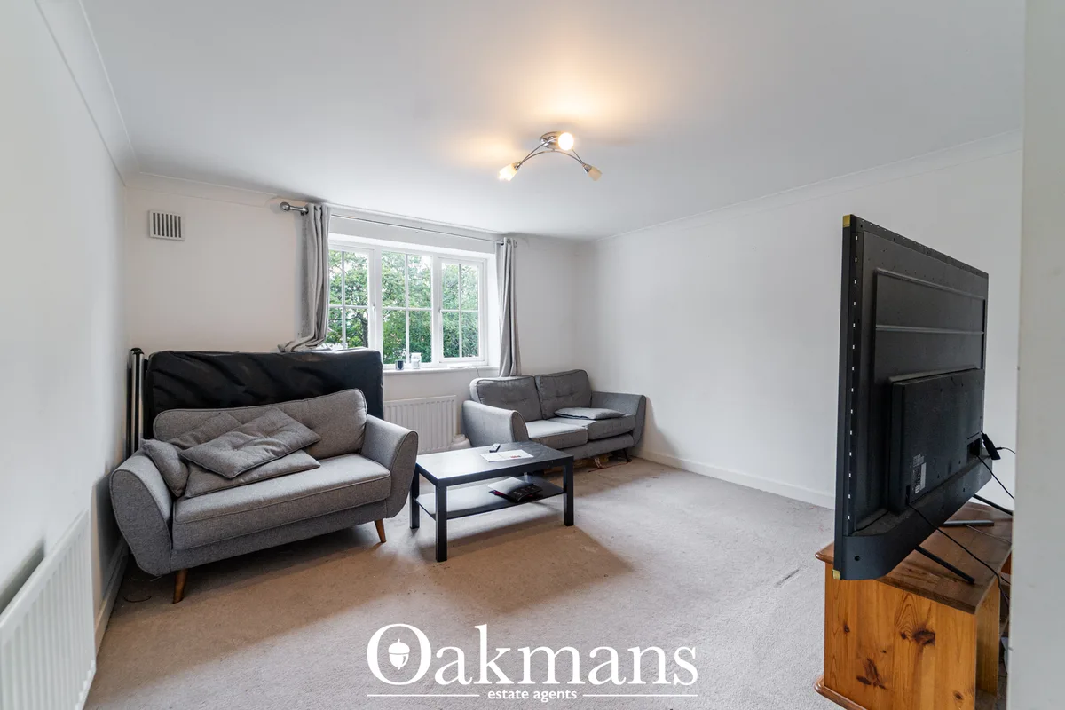 Bright living room with two grey sofas, black coffee table, flat-screen TV on wooden stand, large windows with garden vi