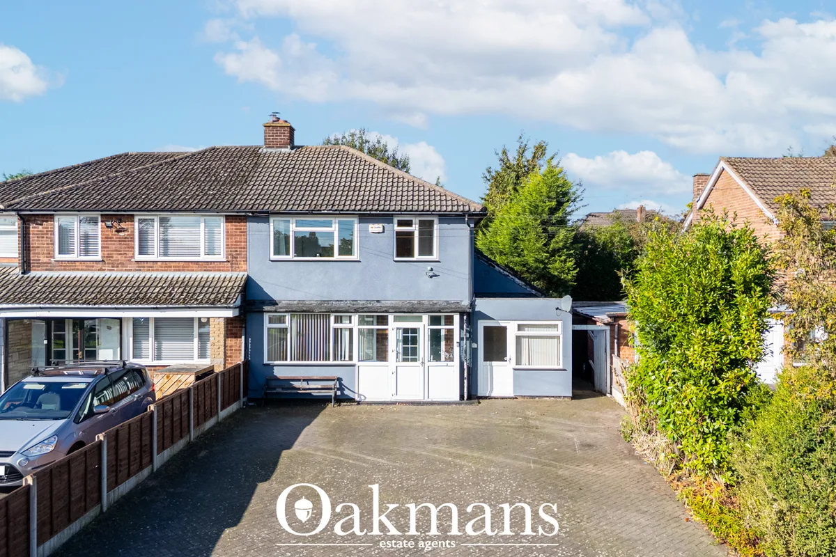 Semi-detached house with blue render, brick chimney, driveway with parked car, mature hedging to boundaries