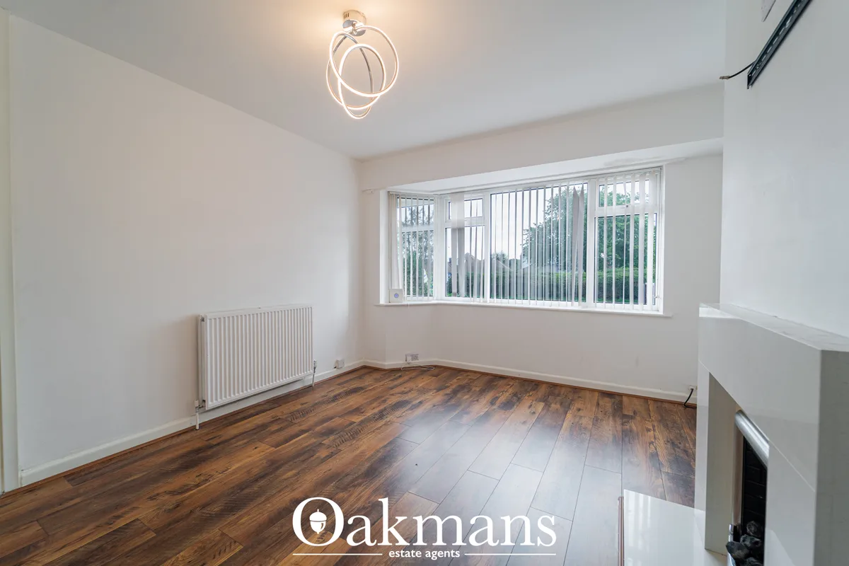 Bright living room with wooden flooring, white walls, radiator, large window with vertical blinds overlooking greenery, 