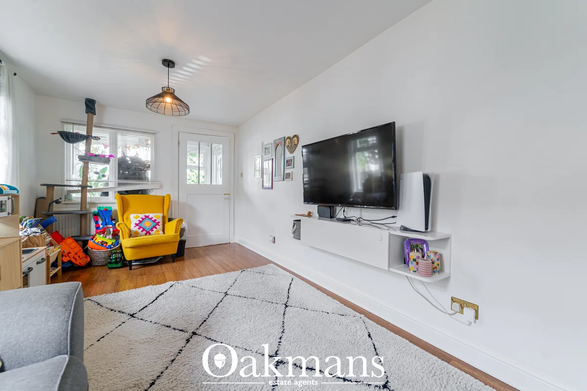 Bright open-plan living room with wall-mounted flat-screen TV, grey patterned rug, yellow armchair, kitchen area and cat