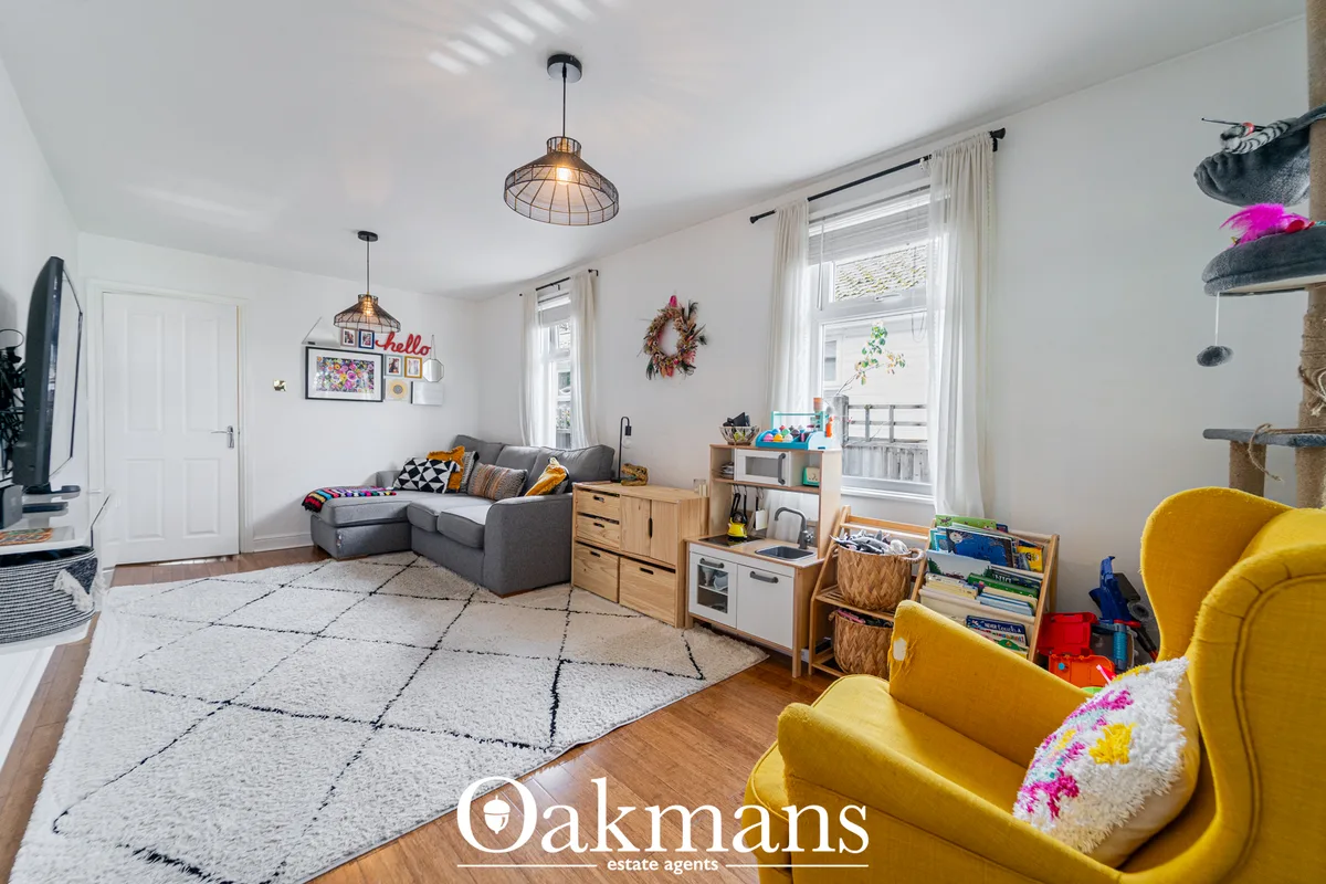 Bright living room with grey sofa, yellow armchairs, wooden storage, pendant lights, patterned rug and large windows wit