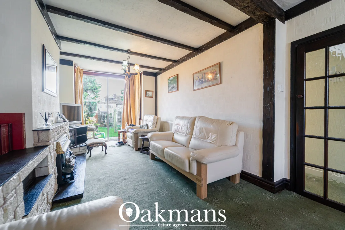 Spacious living room with cream sofa, fireplace, exposed beams, patio doors to garden, artwork on walls