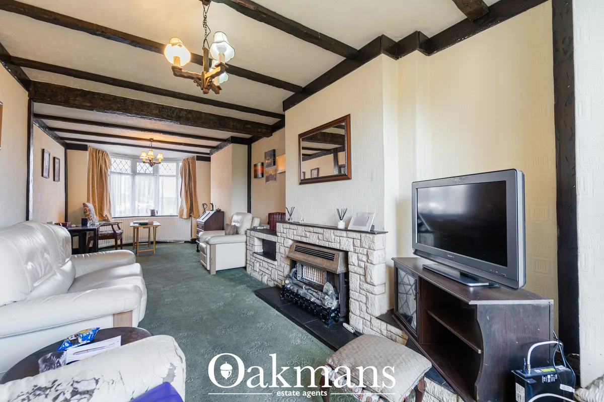 Spacious living room with exposed dark beams, fireplace, cream sofas, flat-screen TV, mirror, and gold curtains