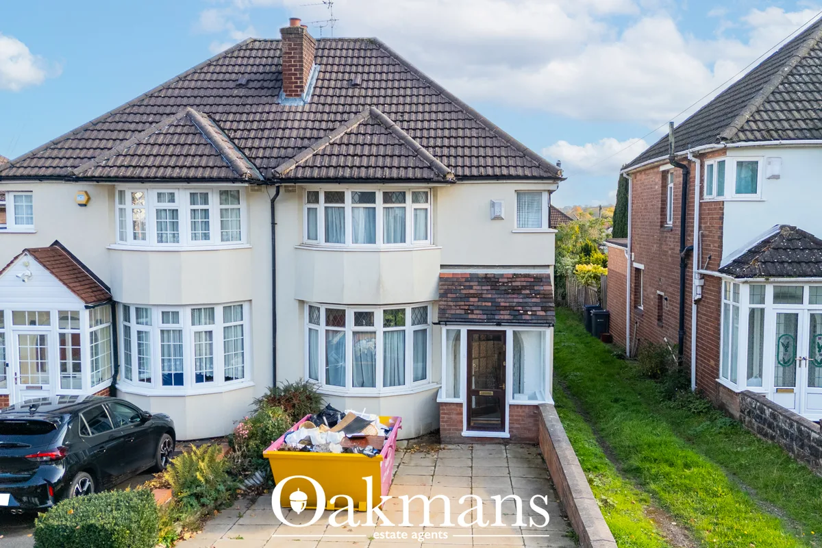 Two-storey detached house with cream render, dark tiled roof, bay windows, driveway with parked car, and neighbouring pr