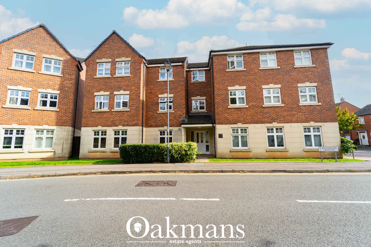 Modern brick apartment building with cream stone base, multiple windows, central entrance, landscaped front garden and s