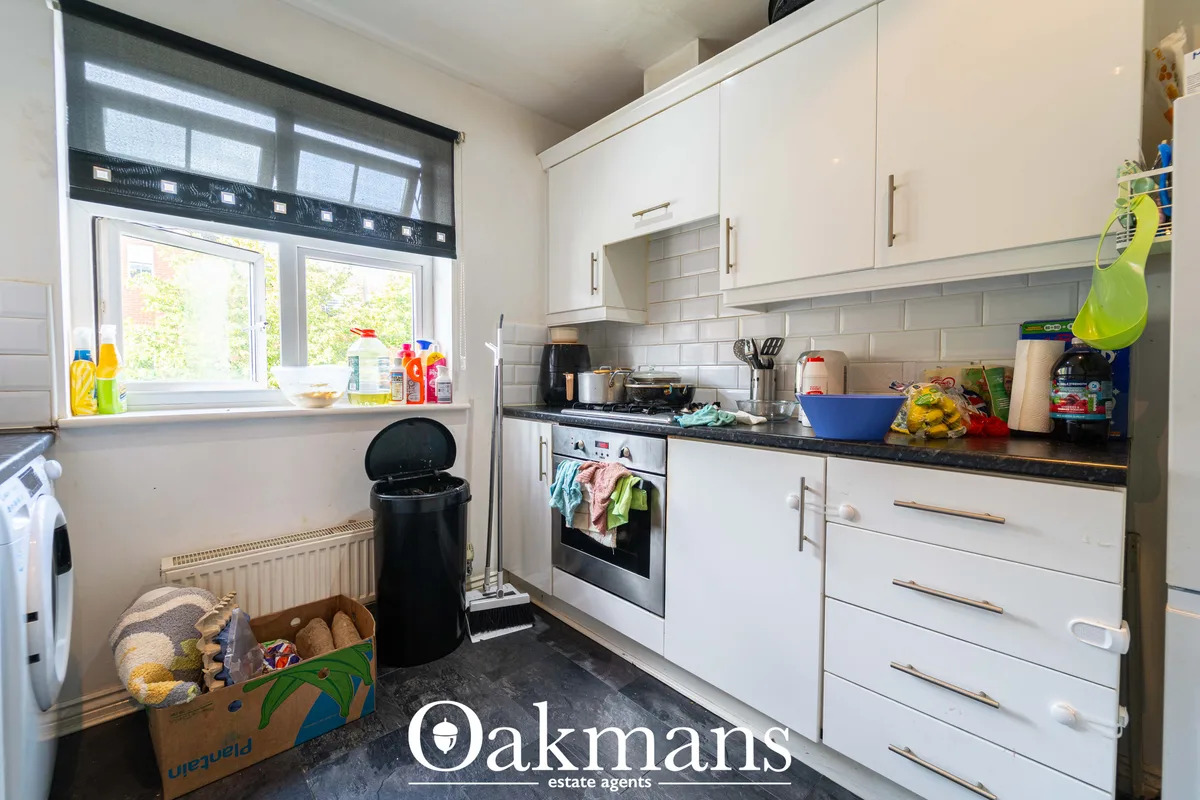 Modern fitted kitchen with white cabinetry, black granite worktops, stainless steel oven, and window overlooking garden
