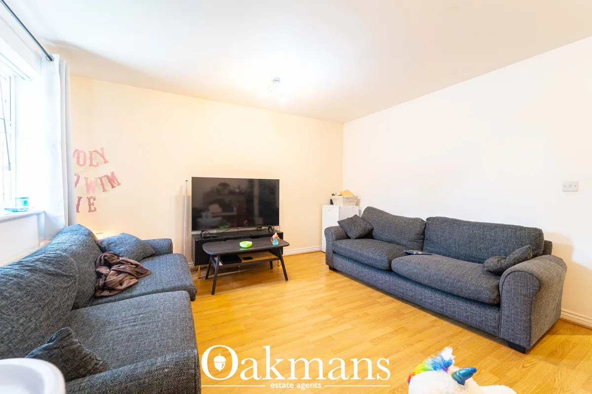 Spacious living room with two grey sofas, wall-mounted TV on black stand, wooden flooring, cream walls and natural light