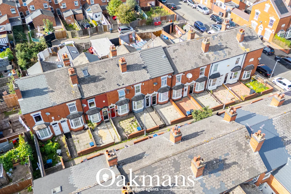 Aerial drone photograph of a row of red-brick terraced houses with slate roofs, small front gardens, parked cars, and su