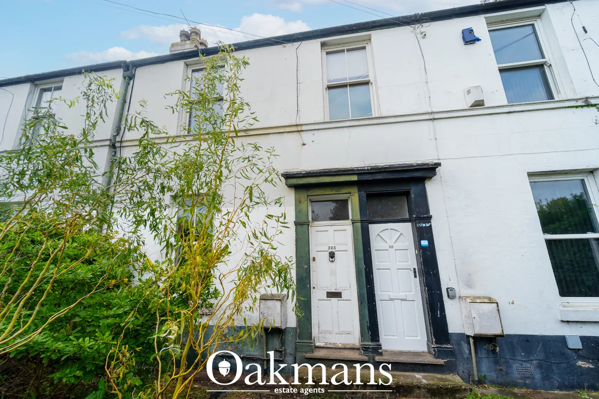 White terraced cottage with dark roof, two front doors, sash windows, climbing vegetation, clear sky