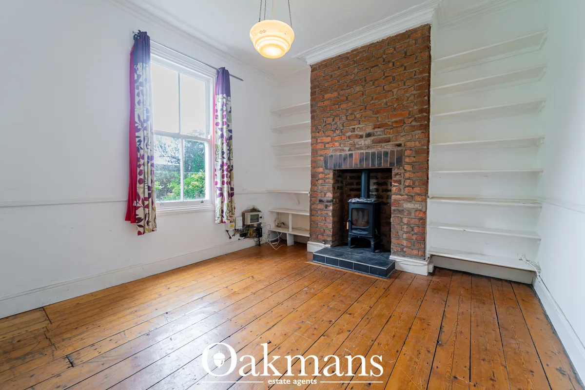 Spacious living room with wooden floorboards, white panelled walls, period fireplace with exposed red brick and wood-bur