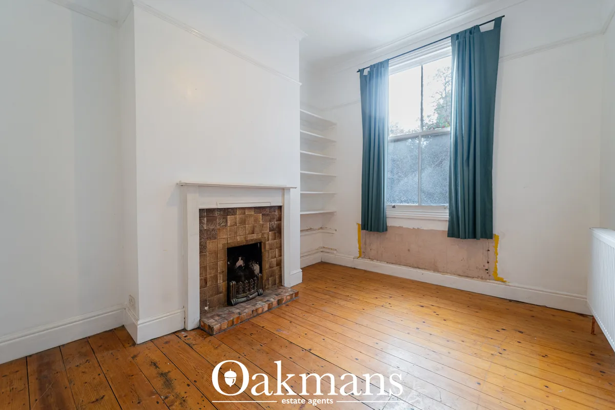 Bright living room with wooden floorboards, white walls, traditional fireplace with brown tiles, built-in shelving, larg