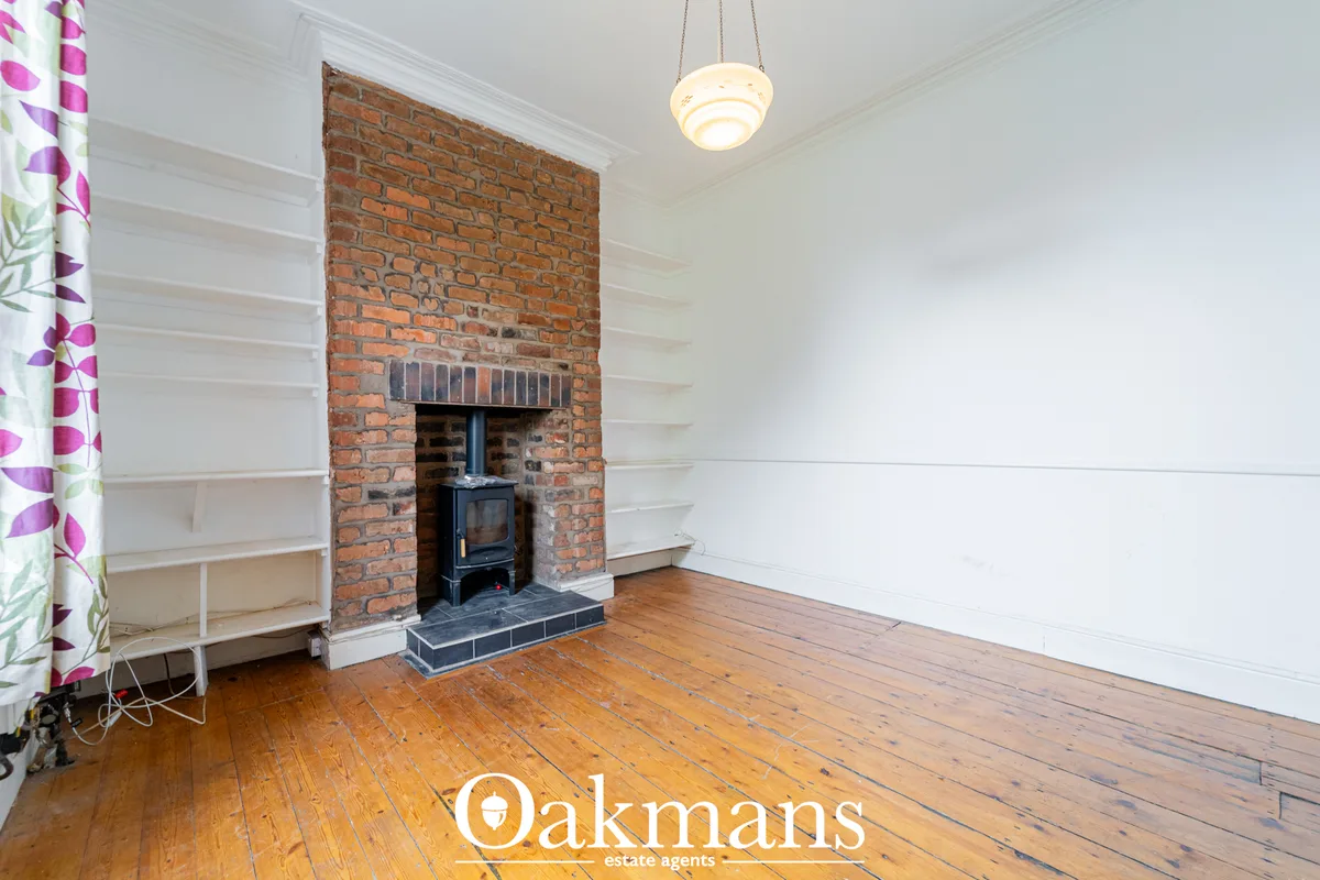 Bright living room with exposed brick fireplace, black wood-burning stove, white built-in shelving, wooden floorboards a