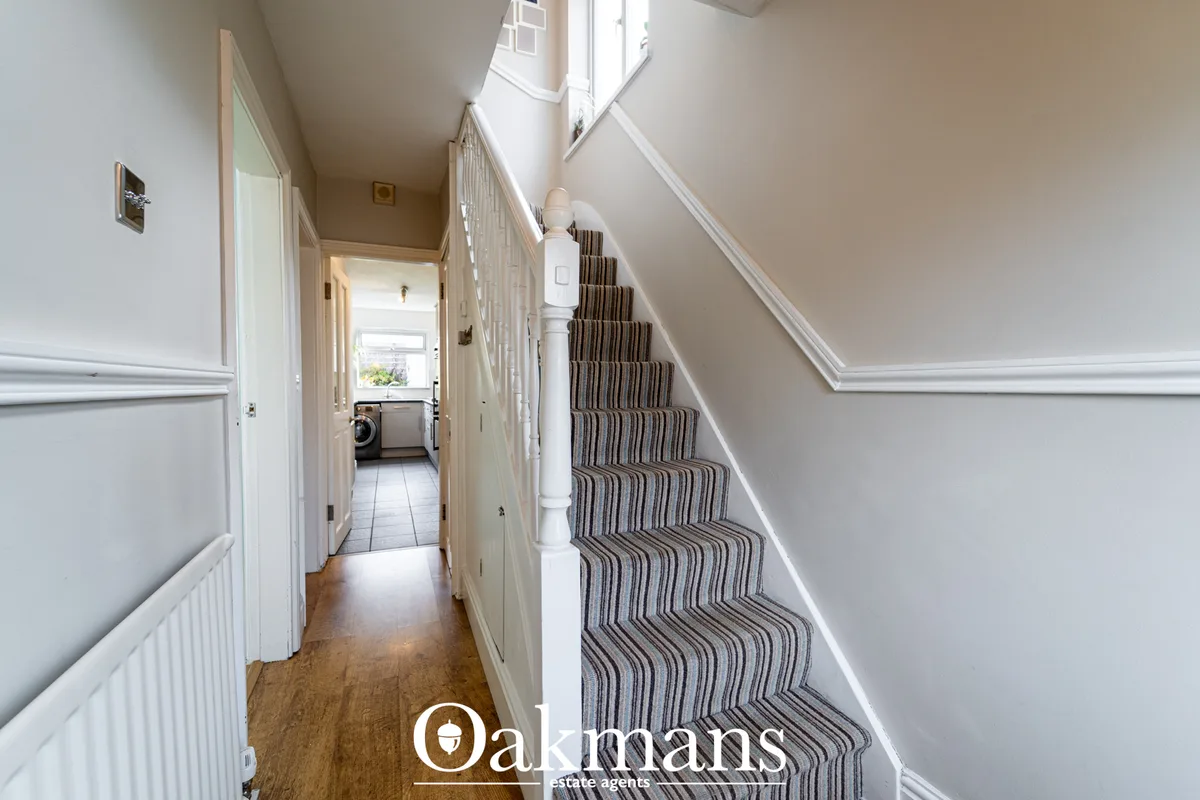 Bright hallway with staircase, striped stair carpet, white railings, wooden flooring, white panelling and natural skylig