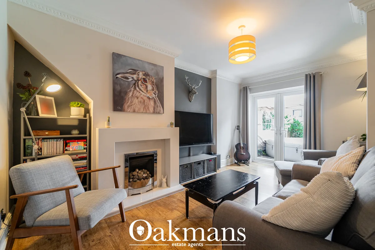 Bright living room with fireplace, TV, grey sofa, mid-century armchair, bookshelves, guitar, and doors opening to garden