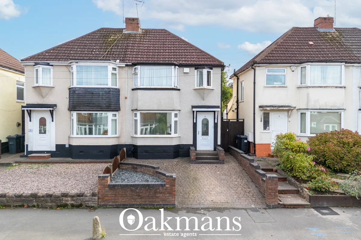 Street-facing view of semi-detached suburban homes with cream and white render, dark tile roofs, bay windows and brick d