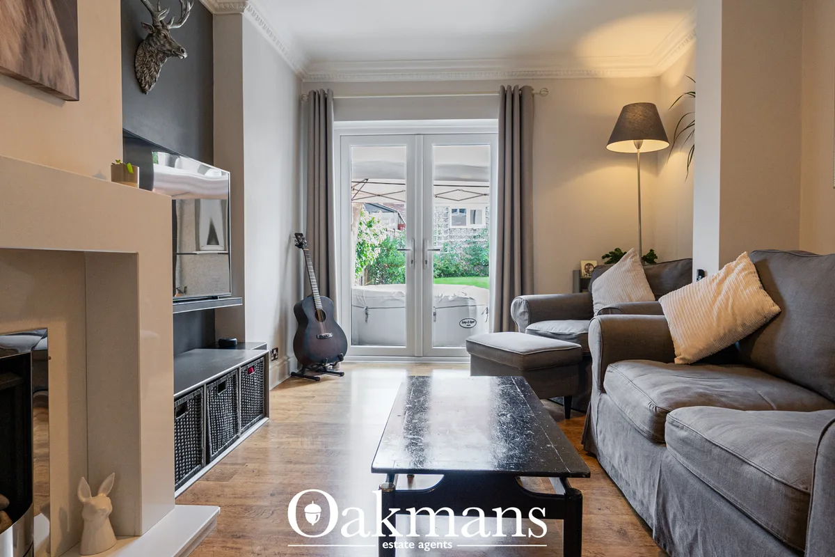 Spacious living room with grey upholstered sofa, coffee table, floor lamp, glass doors to garden, and fireplace with dee