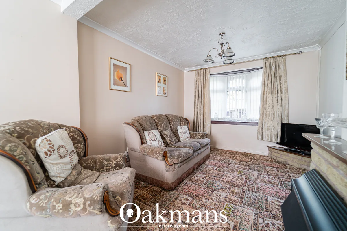 Spacious living room with patterned armchairs, sofa, decorative cushions, patterned rug, window with drapes, framed wall