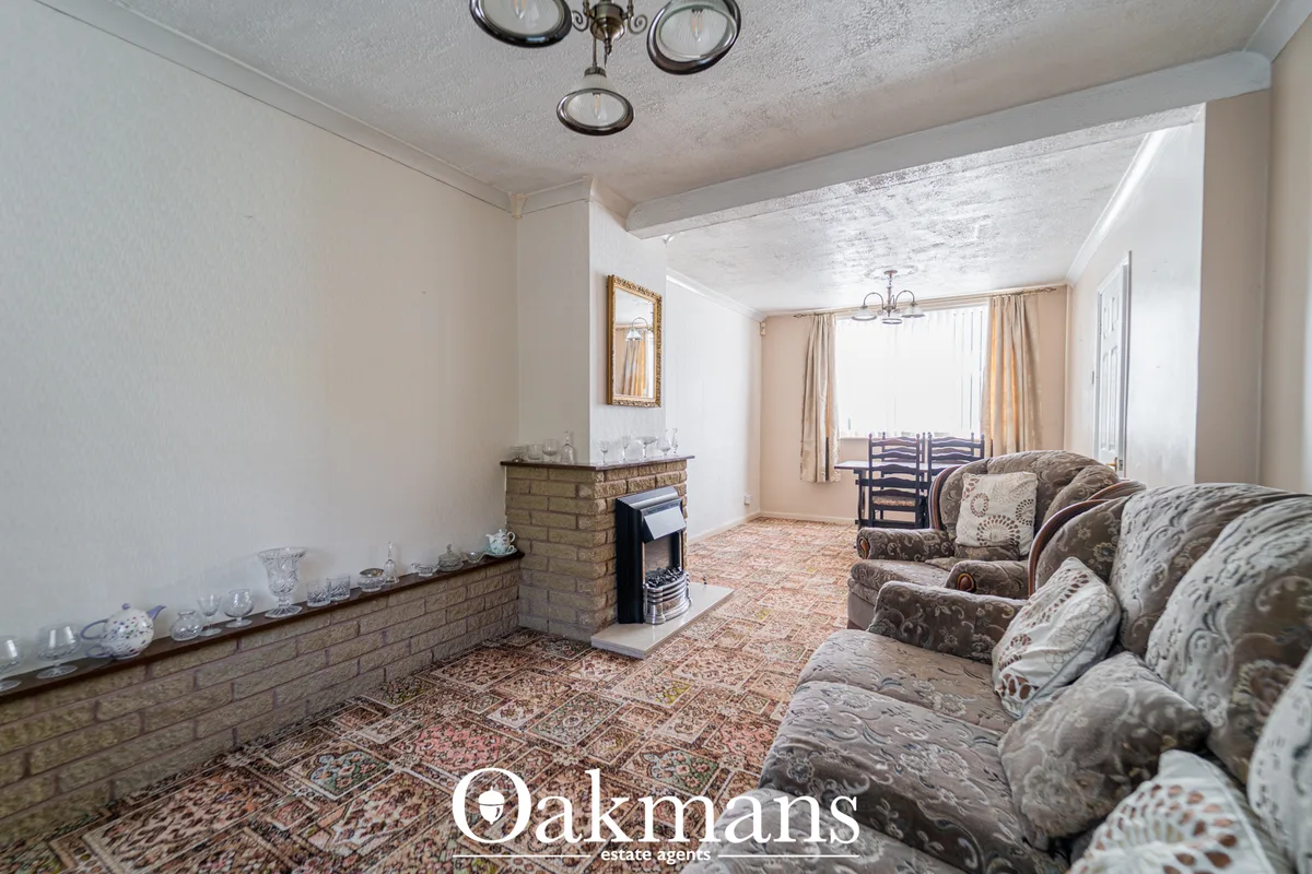 Spacious living room with patterned sofas, fireplace with brick surround, dining area visible through archway, bay windo