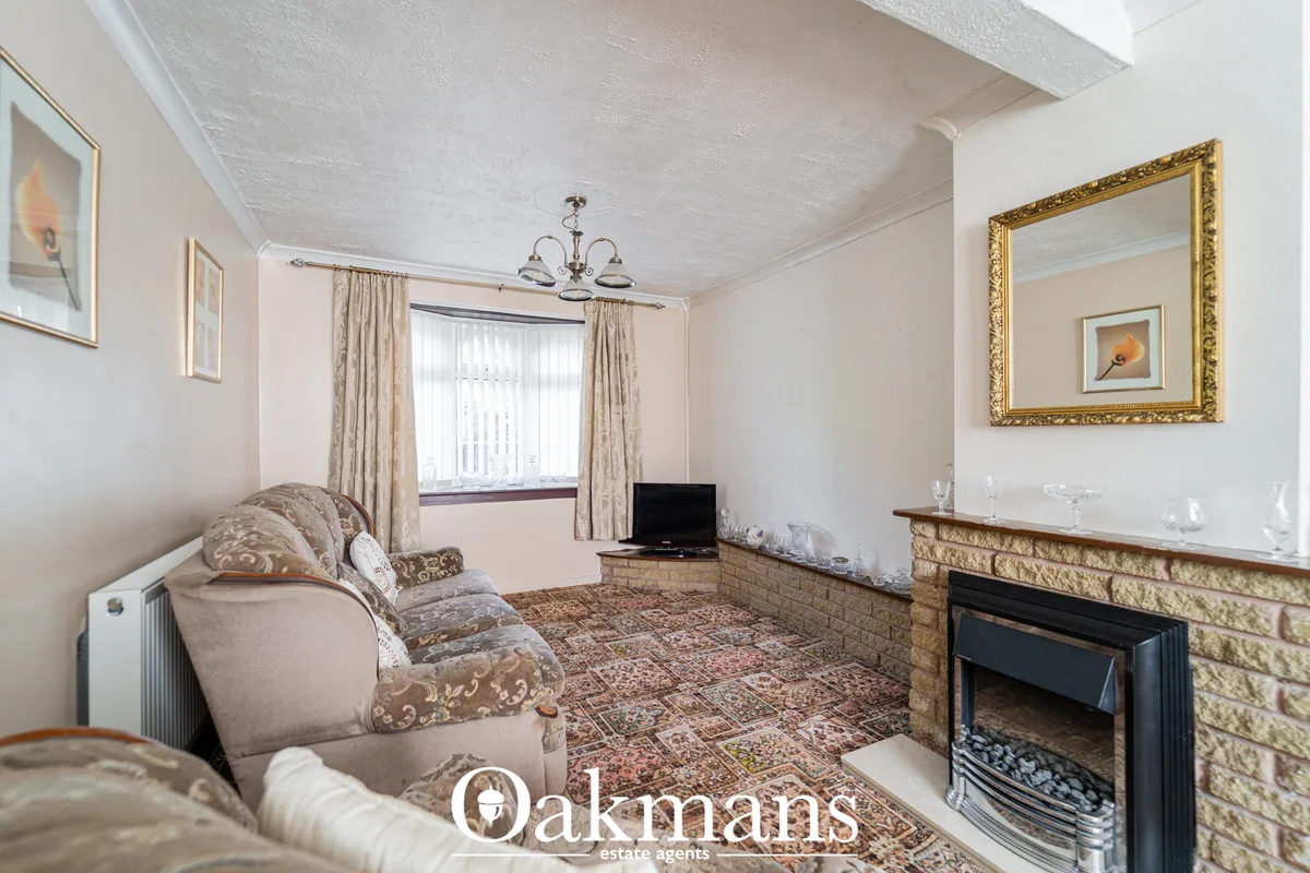 Spacious living room with cream sofa, patterned cushions, fireplace with brick surround, bay window with cream curtains,