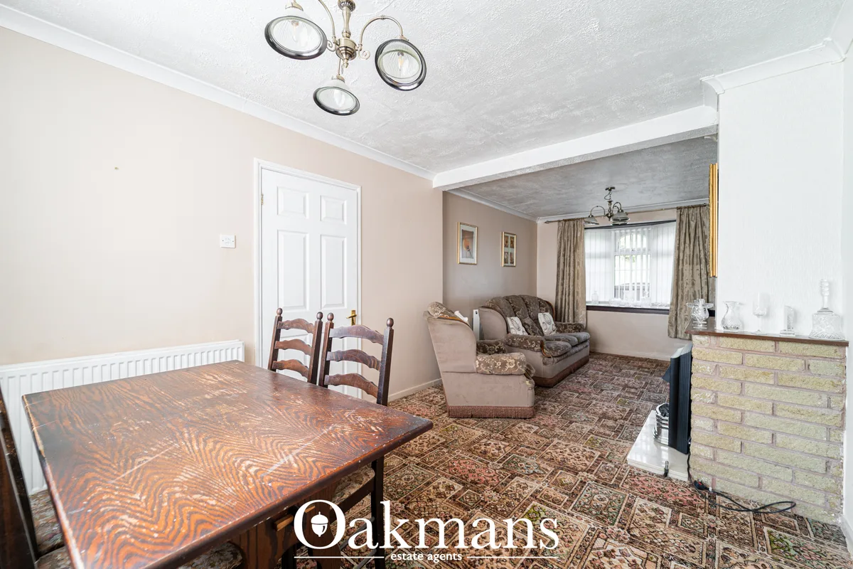 Open-plan living and dining room with peach walls, wooden dining table with chairs, brown upholstered sofa and armchair,