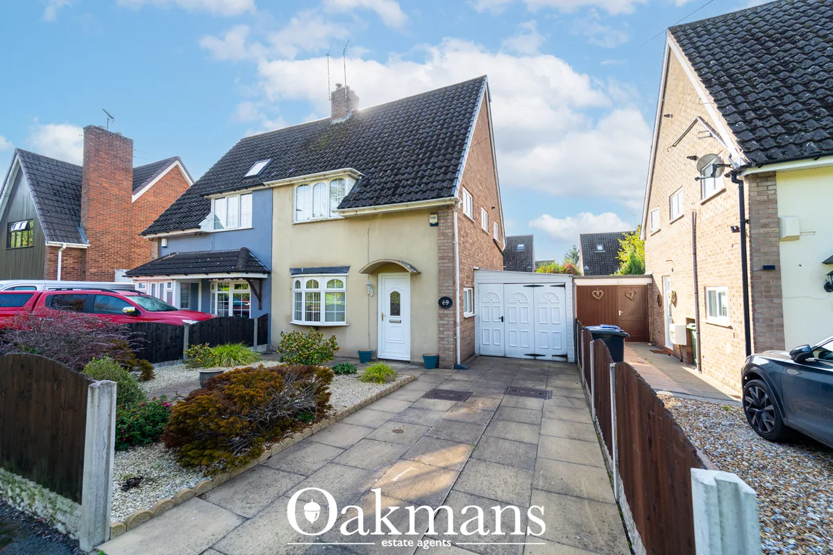 Brick detached house with cream render, dark tiled roof, white garage door, driveway and front garden with shrubs