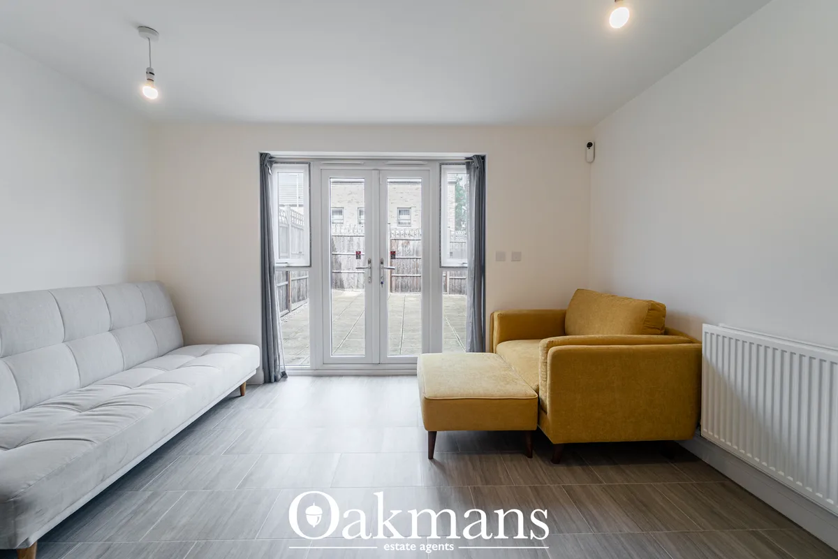 Bright living room with light grey sofa on left, mustard armchair and footstool on right, French doors opening onto balc