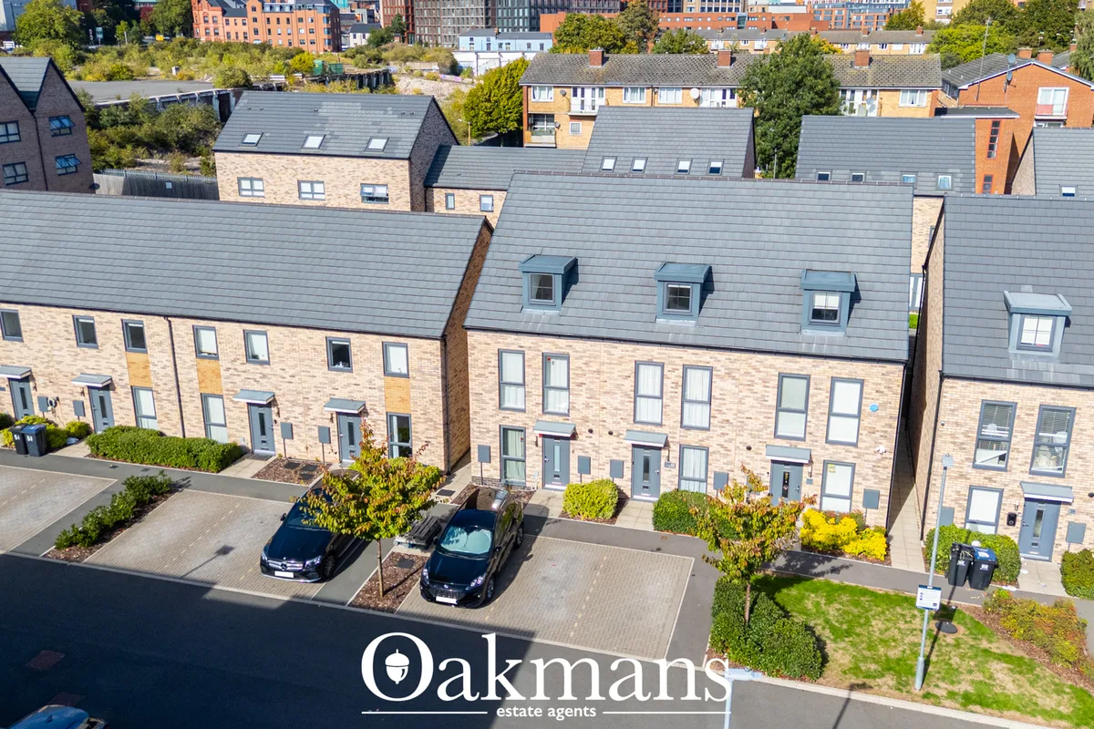 Aerial view of modern brick townhouses with slate roofs, driveways, manicured gardens and urban backdrop