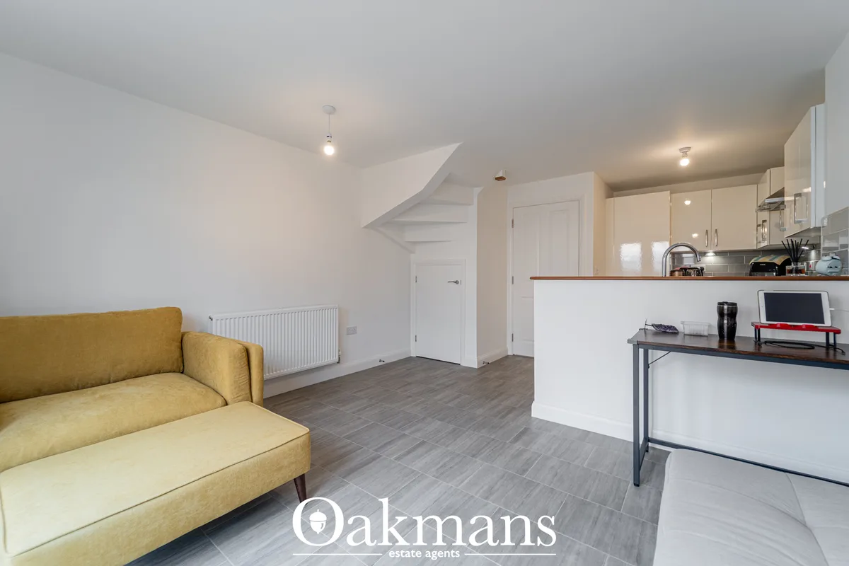 Open-plan living space with mustard yellow sofa, white kitchen units, wooden breakfast bar and stairs to upper floor