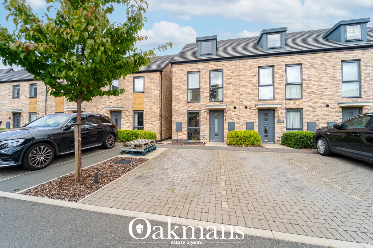 Modern brick townhouses with mansard roofs, parked cars, paved courtyard and mature tree